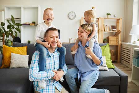 Family laughing in their living room with father and mother hold their son and daughter on their shoulders