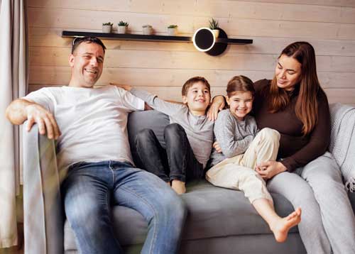 Happy family relaxing together on a comfortable gray couch in their living room, enjoying a safe and cozy environment with reliable HVAC, plumbing, and electrical systems