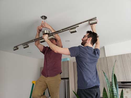 Electricians installing a modern ceiling light fixture during a home lighting upgrade