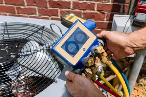 Technician testing the air conditioner condenser outside of a brick home