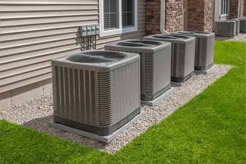 Row of ac condensers in a gravel section of yard outside suburban townhomes